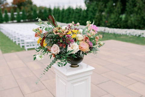 Image of fall wedding ceremony flower arrangement on pedestal at the Cape Club of Sharon, a Massachusetts wedding venue. The image shows the flower arrangement on top of the pedestal with the ceremony space in the background.