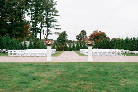 Image of outdoor ceremony set up at the Cape Club of Sharon, a Massachusetts wedding ceremony. The image shows lush green grass with white garden chairs on either side of the paved asile.