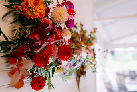 Image of statement wedding ceremony flowers, wal flroal installation in muted fall colros including dahlias, marigolds, sedum, celosia, ranunculus, lisianthus, mums, leucadendron, asclepia, eucalyptus, and amaranthus.