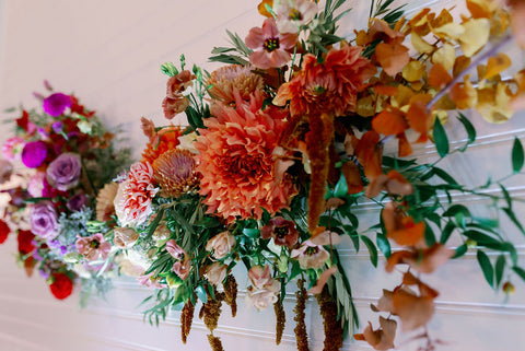 Image of wedding reception wall floral installation in muted fall colors including dahlias, marigolds, sedum, celosia, ranunculus, lisianthus, mums, leucadendron, asclepia, eucalyptus, and amaranthus.