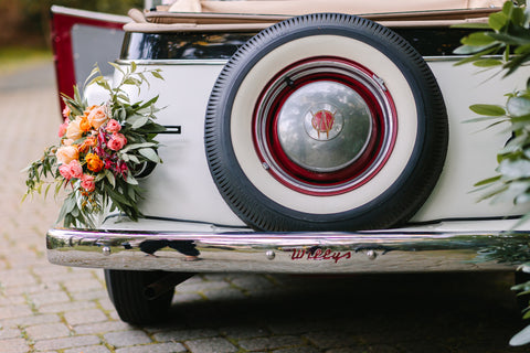 Image of a vintage rental car adorned with a floral design including roses and ranunculus in shades of orange.