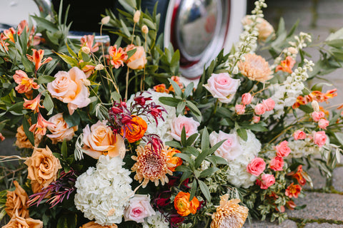 Image of a stunning flower arrangement including hydrangeas, roses, dahlias and greenery. The flowers are vibrant with shades of orange and other early fall colors.