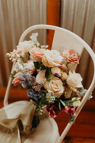 Image of a bride's bridal bouquet with pale pink roses, blue delphinium, and more for a rustic elegant wedding