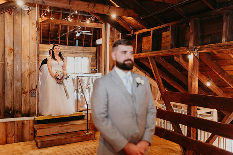 Image of bride coming in to meet her groom in a rustic barn for their first look