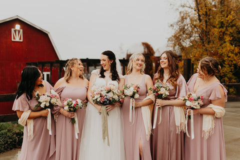 Picture of bridal party holiday dusty pink rose wedding bouquets with matching pink bridesmaid dresses in front of rusticred barn brewery