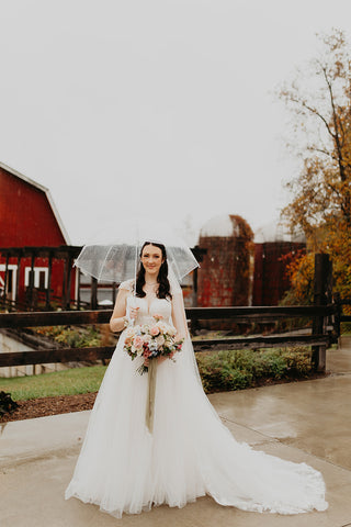 Picture of bride holding her rustic elegant bridal bouquet in front or a red barn