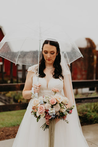 Image of bride holding a lush textured bridal bouquet featuring soft pink roses in front of a rustic barn