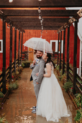 Picture of bride and groom inder umbrella in front of rustic red barn at Westfield River Breing Company in Southwick, MA