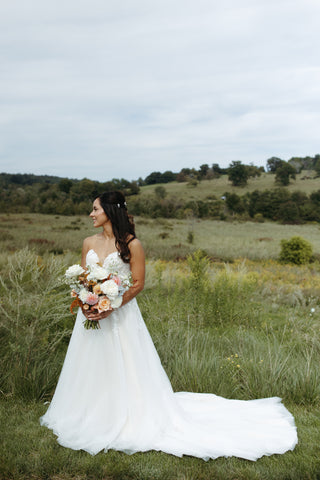 late summer wedding bride carrying a bouquet  with timeless flowers and modern foliage including roses, dahlias, delphinium, dyed grevillea, rice flower, cress, and thistle