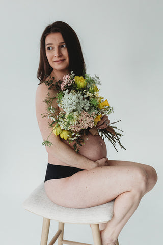 Image of mom to be during a styled maternity photoshoot holding a wild, organic bouqueet of loose white and yellow flowers.