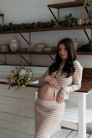 Image of mom to be during a styled maternity photoshoot holding a wild, organic bouqueet of loose white and yellow flowers.