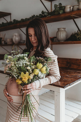 Image of mom to be during a styled maternity photoshoot holding a wild, organic bouqueet of loose white and yellow flowers.