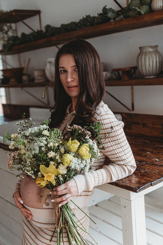 Image of mom to be during a styled maternity photoshoot holding a wild, organic bouqueet of loose white and yellow flowers.