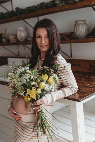 Image of mom to be during a styled maternity photoshoot holding a wild, organic bouqueet of loose white and yellow flowers.