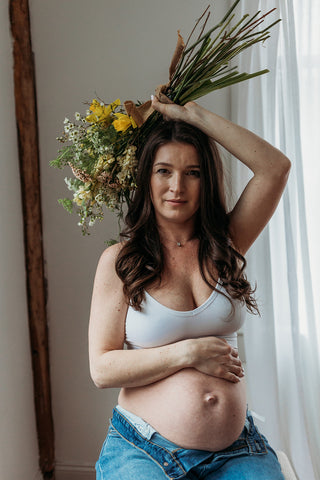 Image of mom to be during a styled maternity photoshoot holding a wild, organic bouqueet of loose white and yellow flowers.