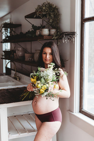 Image of mom to be during a styled maternity photoshoot holding a wild, organic bouqueet of loose white and yellow flowers.