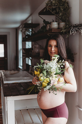 Image of mom to be during a styled maternity photoshoot holding a wild, organic bouqueet of loose white and yellow flowers.