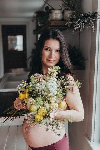 Image of mom to be during a styled maternity photoshoot holding a wild, organic bouqueet of loose white and yellow flowers.