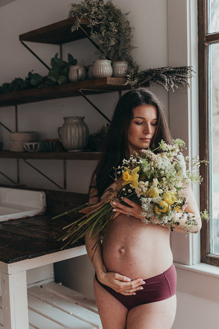 Image of mom to be during a styled maternity photoshoot holding a wild, organic bouqueet of loose white and yellow flowers.