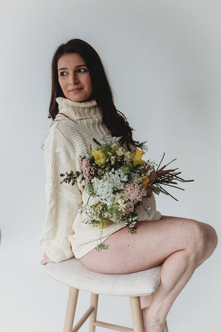 Image of mom to be during a styled maternity photoshoot holding a wild, organic bouqueet of loose white and yellow flowers.