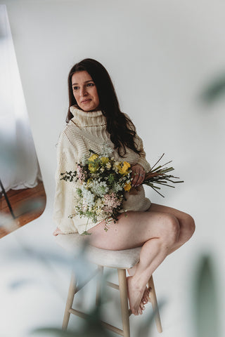 Image of mom to be during a styled maternity photoshoot holding a wild, organic bouqueet of loose white and yellow flowers.