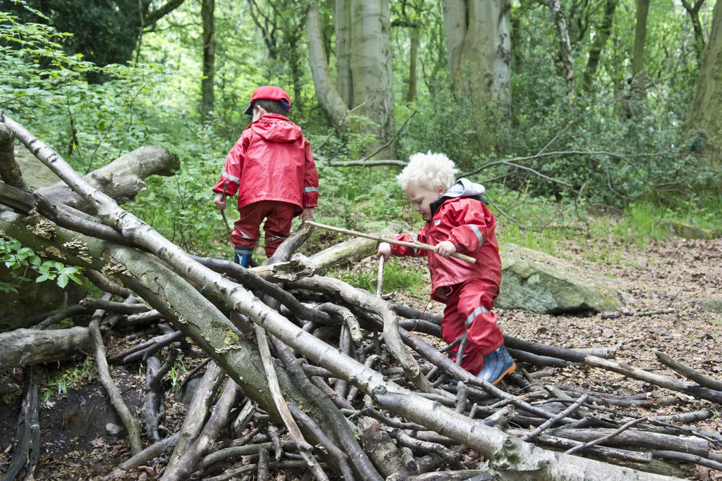 Children in red raincoats building a structure with sticks in a forest.