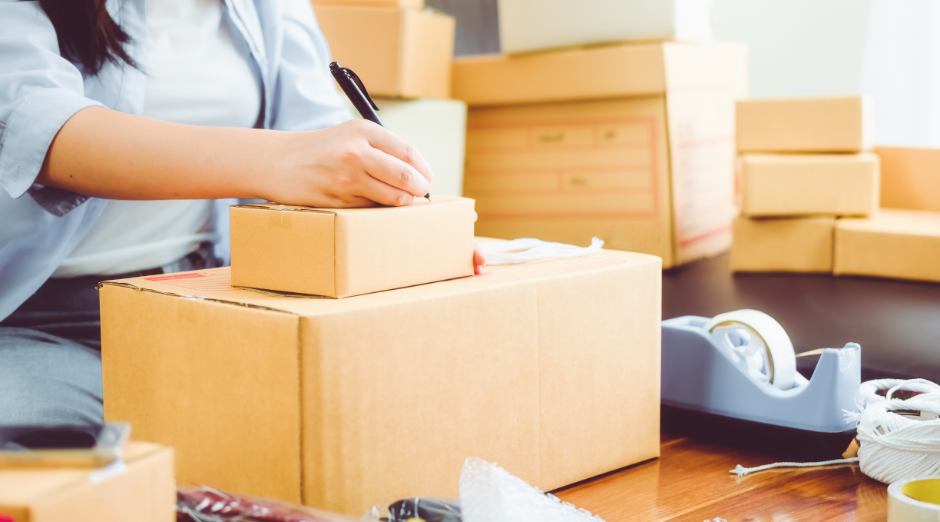 woman packing products into a cardboard box, preparing it for shipping.