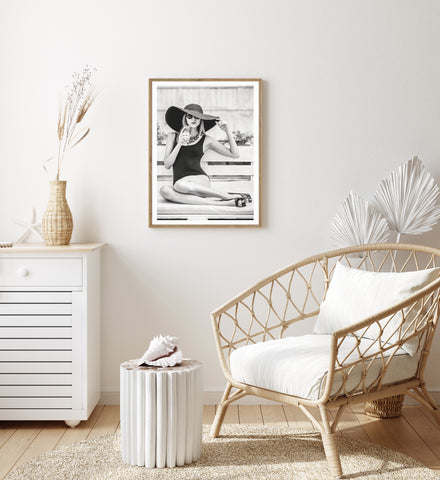 Black and white photography wall art of a woman relaxing in the sun. Pictured in a neutral bedroom. 