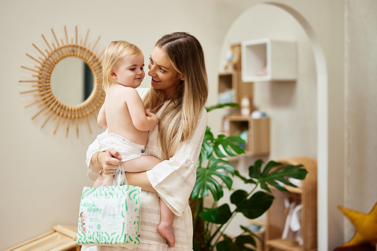 A woman holding a toddler in a modern room with plants and decor.