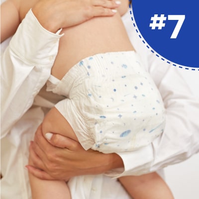 A close-up of a baby being held, wearing a diaper and a partial view of an adult's arms.