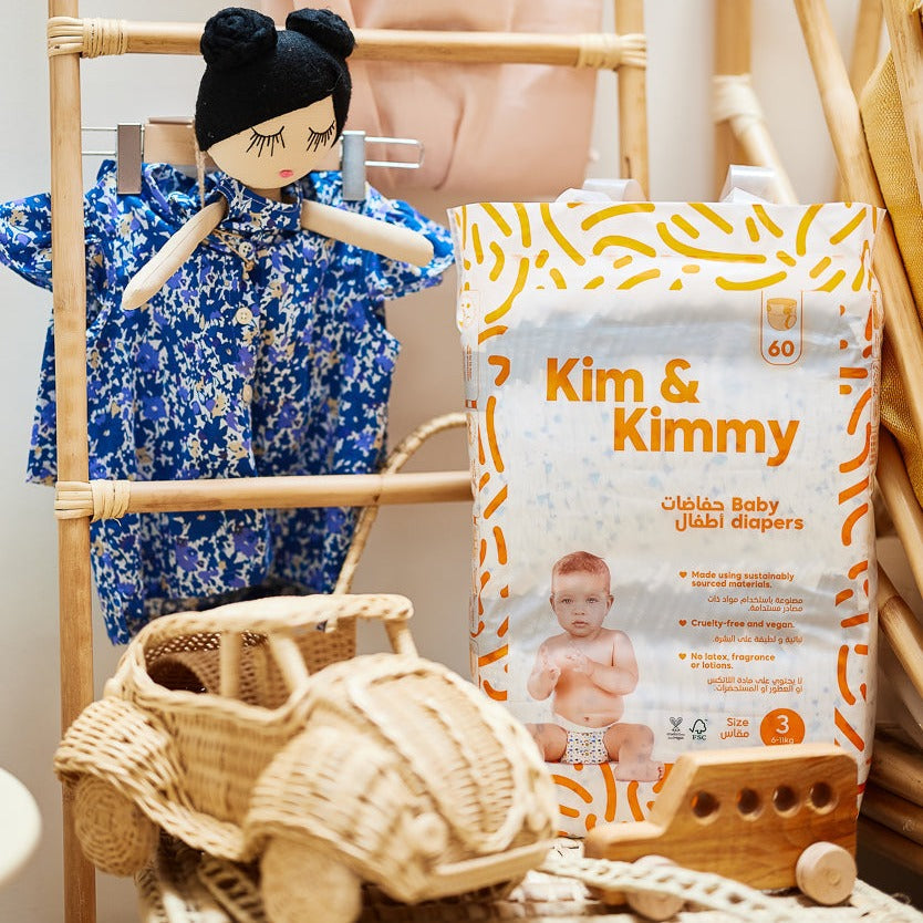 Pack of baby diapers next to a doll and wicker accessories on shelves.