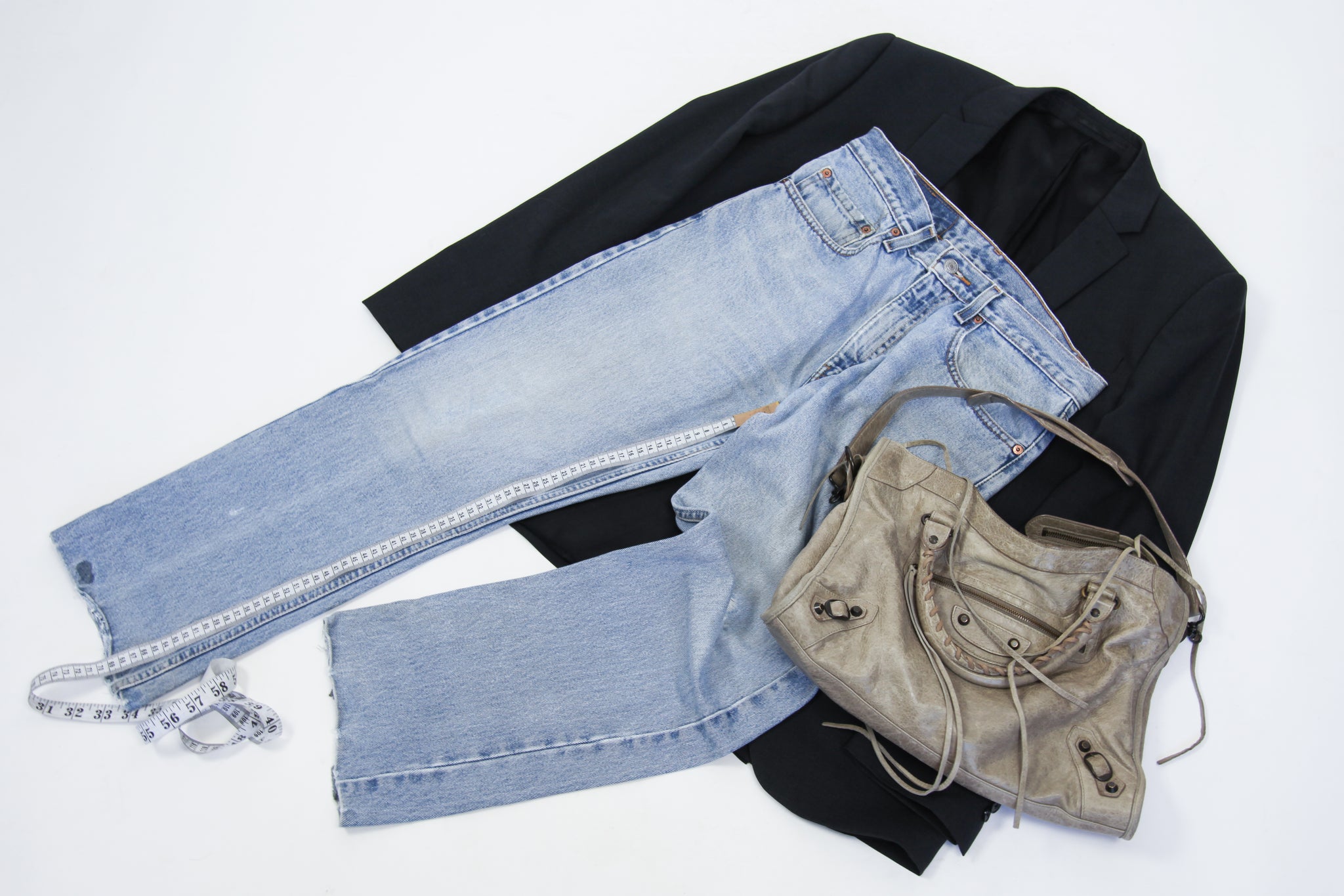 Flat lay of blazer, bag and jeans with measuring tape on inside leg