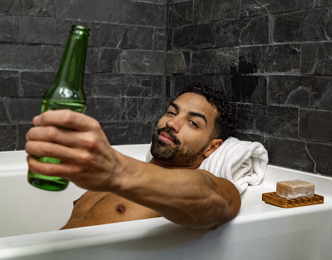 Male model in bath tub holding a beer