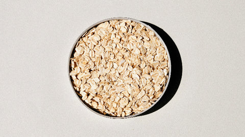 A bowl filled with rolled oats, viewed from above on a neutral background, illustrating the primary ingredient used in a natural oatmeal face mask for skin care.