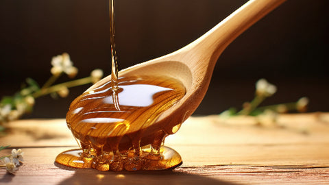 Golden honey dripping from a wooden spoon onto a rustic surface, representing a natural ingredient for skin care with its moisturizing and antibacterial properties.