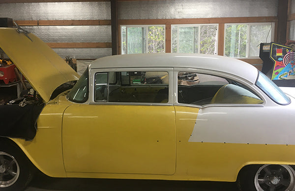 A classic yellow car with the hood open. The car is parked in a garage.