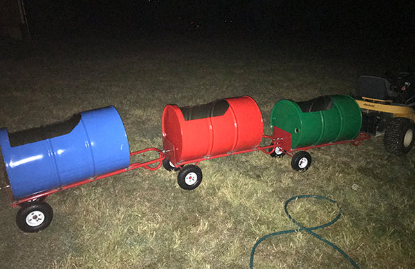 A series of barrels that have been turned into train cars for children to ride in, as they are pulled behind a tractor.