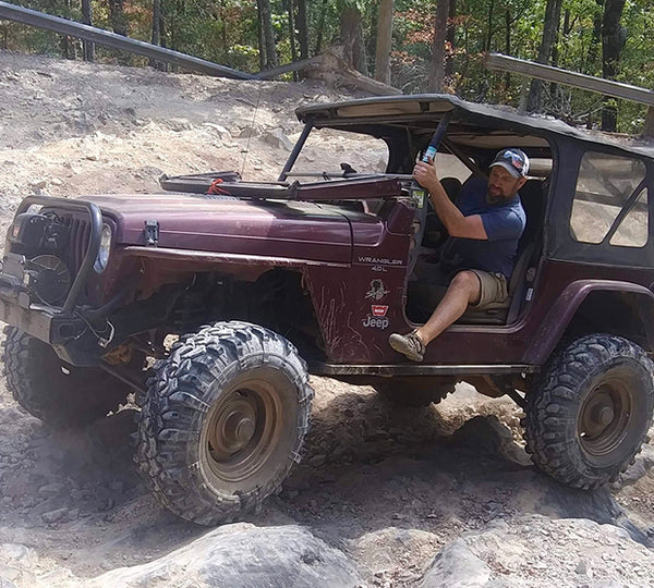 A man drives a Jeep on a dirt road.