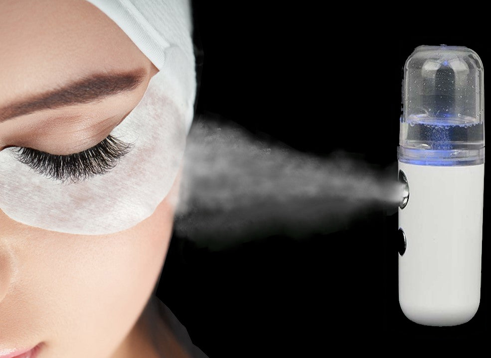 a nano mister device emitting a fine mist, directed towards a client's eye/face during a beauty treatment. The mist provides hydration and sets products, enhancing the comfort and effectiveness of the lash extension procedure