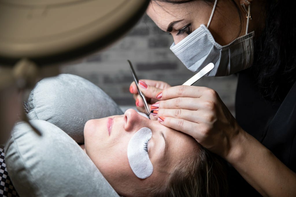 A professional technician using tweezers to perform eyelash extension application on a woman, ensuring precise and meticulous lash placement.