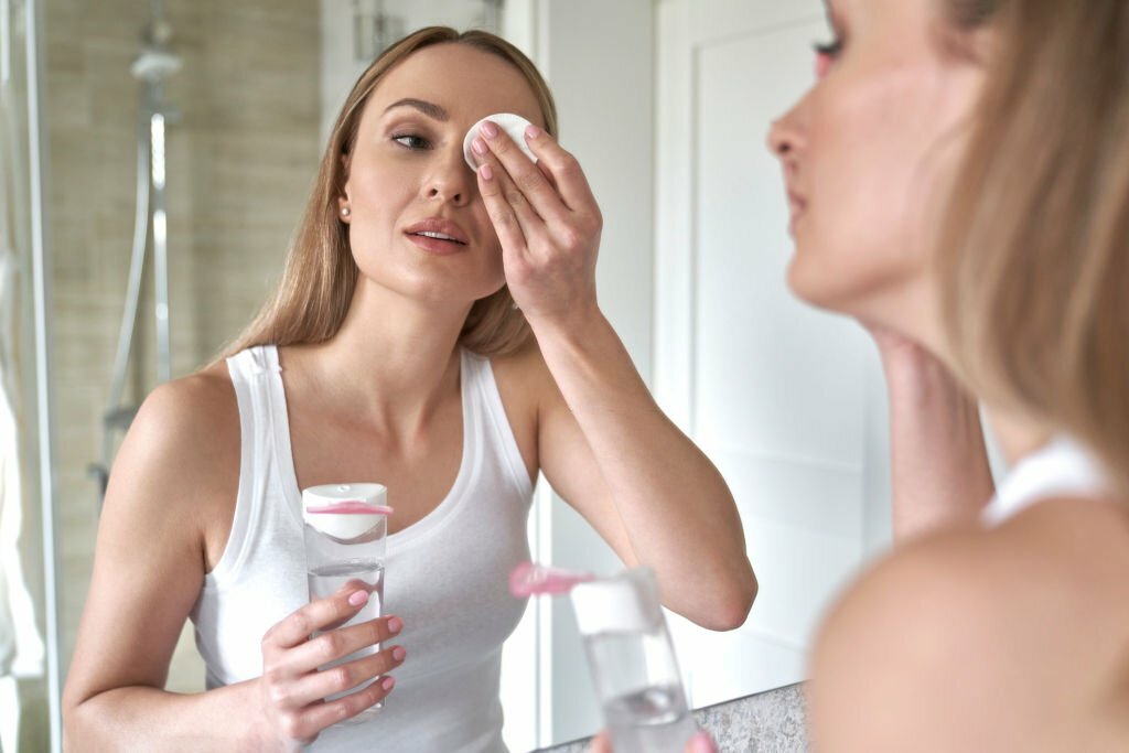 A woman removing eye makeup with oil-free eye makeup remover and a lint-free cotton pad by gently swiping the pad over her lashes and eyelids