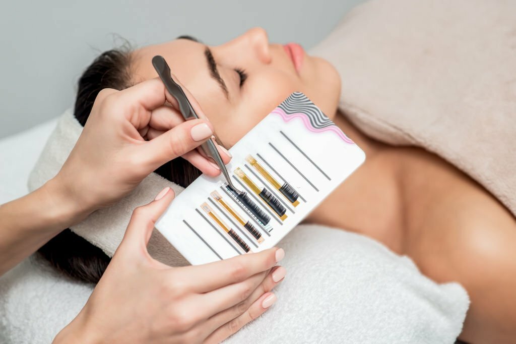 A lash technician skillfully using tweezers to organize various lash strips on a specialized lash tile