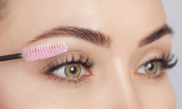 An image of a woman delicately brushing her eyelashes as part of her lash aftercare routine, ensuring the extensions remain neat and separated