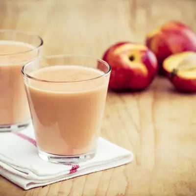 Zwei Gläser Apfelsaft auf einem Geschirrtuch auf einem hölzernen Tisch mit roten Äpfeln im Hintergrund, einer davon halbiert.
