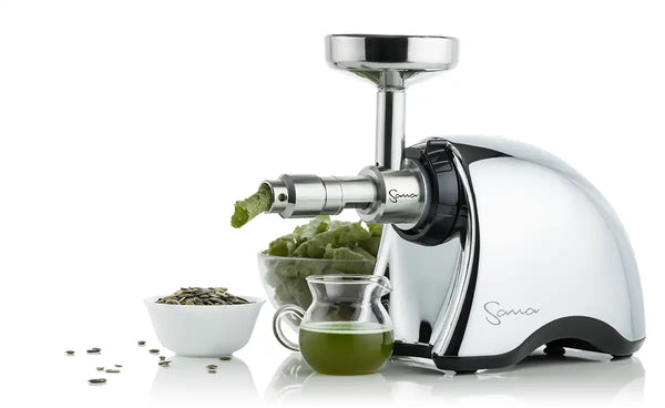 Der Sana 707 Slow Juicer mit dem Sana 702 Ölpresse-Ansatz presst Kürbiskerne. Neben der Saftpresse befinden sich eine Schüssel mit Kürbiskernen und ein halb gefüllter Behälter mit Kürbiskernöl.