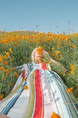 Girl in a rainbow striped dress lying in a meadow looking at the sky