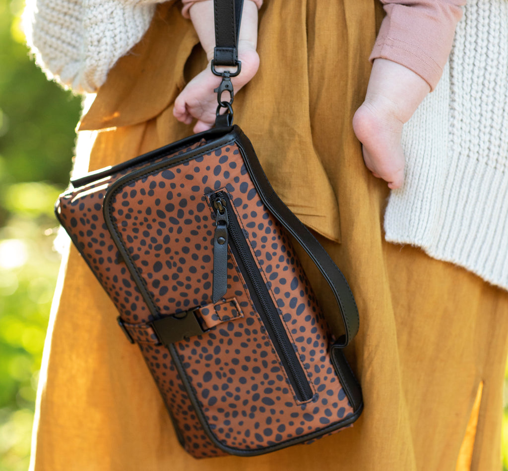 woman holds baby and dockatot leopard print clutch changing bag