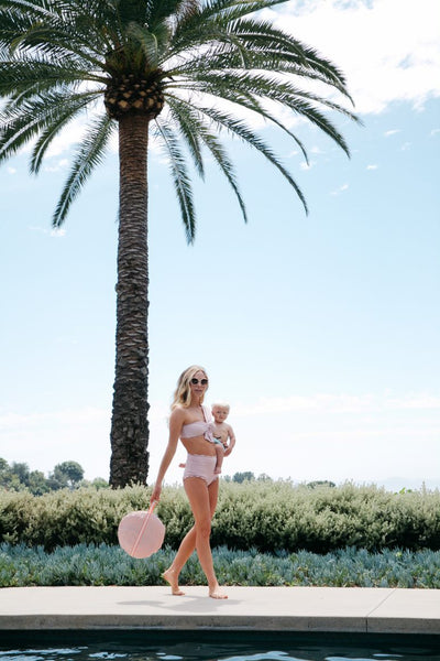 woman carrying her baby and DockATot Cabana Kit in carry pouch alongside a pool