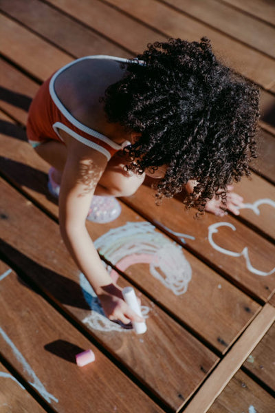 Little Girl drawing with chalk on wooden decking