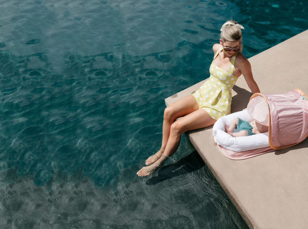 Woman dipping her toes into a pool with a baby lounging in a DockATot Deluxe+ dock with Cabana Kit